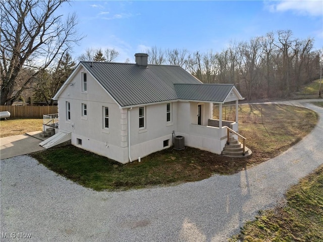 view of side of property with central AC unit, fence, metal roof, and stucco siding