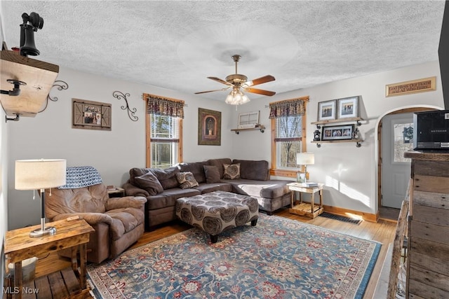 living room with ceiling fan, a textured ceiling, arched walkways, and wood finished floors