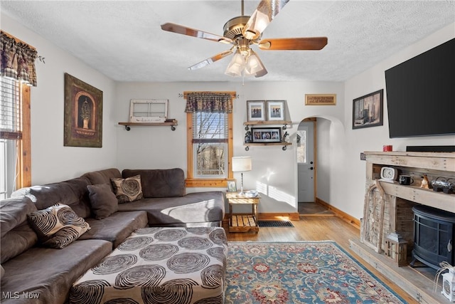 living room with baseboards, arched walkways, a ceiling fan, wood finished floors, and a textured ceiling