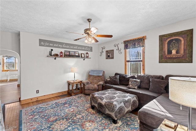 living area featuring baseboards, arched walkways, a ceiling fan, hardwood / wood-style floors, and a textured ceiling