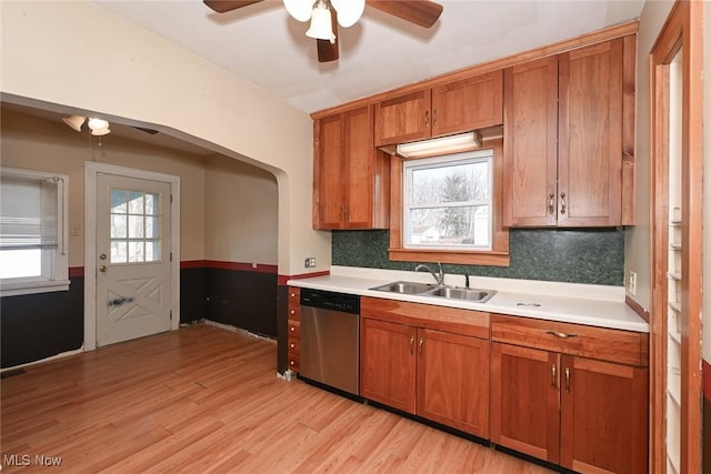 kitchen with dishwasher, light wood-style flooring, brown cabinets, light countertops, and a sink