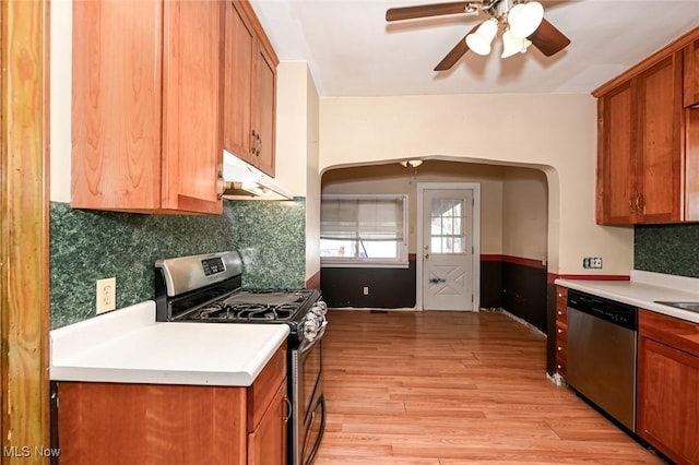 kitchen featuring arched walkways, under cabinet range hood, light wood-style floors, light countertops, and appliances with stainless steel finishes