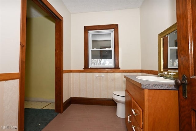 half bathroom with a textured ceiling, toilet, a wainscoted wall, wood finished floors, and vanity