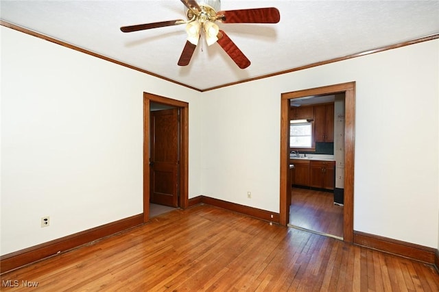 empty room featuring ornamental molding, ceiling fan, light wood finished floors, and baseboards