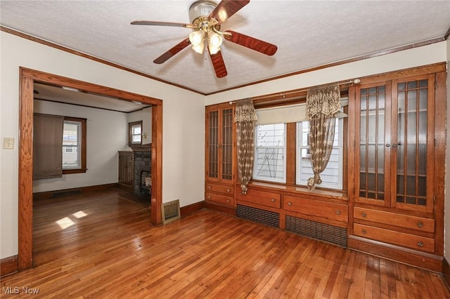 empty room featuring a fireplace, visible vents, ornamental molding, a textured ceiling, and hardwood / wood-style flooring