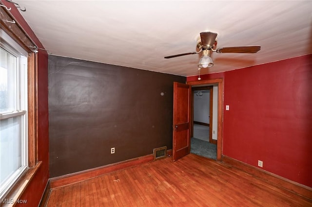 unfurnished room with a ceiling fan, visible vents, baseboards, and wood finished floors