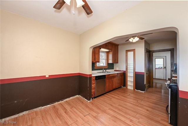 kitchen featuring arched walkways, appliances with stainless steel finishes, light countertops, light wood-type flooring, and a sink