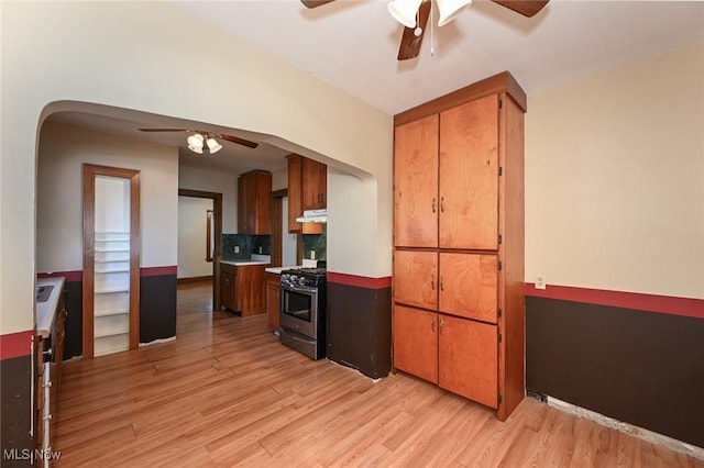 kitchen featuring light wood-style floors, gas range, ceiling fan, brown cabinets, and under cabinet range hood