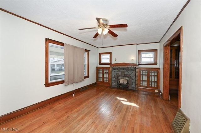 unfurnished living room with baseboards, wood-type flooring, crown molding, a textured ceiling, and a fireplace