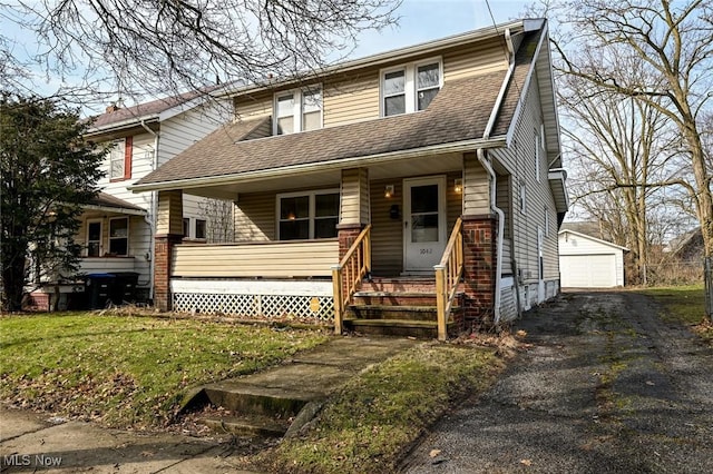 view of front of house with an outbuilding, a detached garage, a shingled roof, covered porch, and a front yard