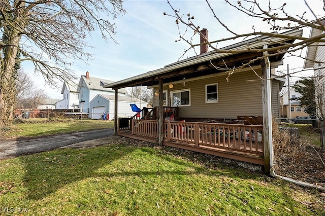 back of house featuring a chimney, fence, aphalt driveway, and a lawn