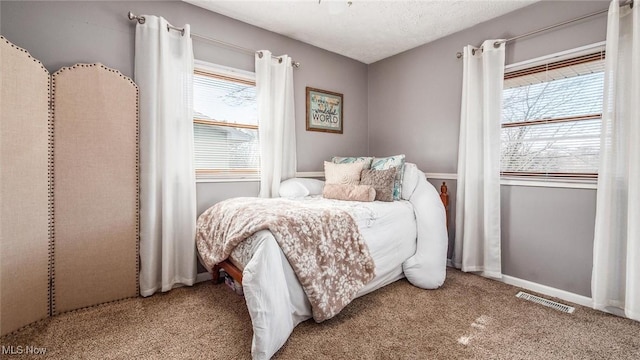 bedroom with carpet flooring, visible vents, a textured ceiling, and baseboards