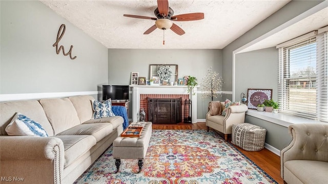 living area with ceiling fan, a textured ceiling, baseboards, and wood finished floors