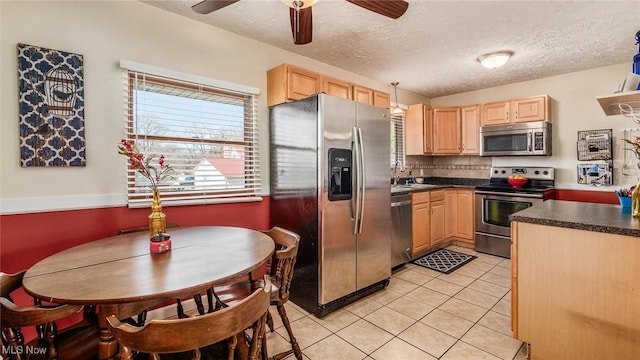 kitchen with light tile patterned floors, stainless steel appliances, dark countertops, decorative backsplash, and light brown cabinets