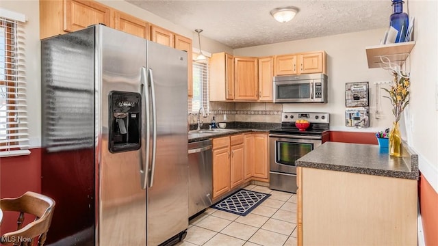 kitchen featuring dark countertops, appliances with stainless steel finishes, light brown cabinetry, a sink, and light tile patterned flooring