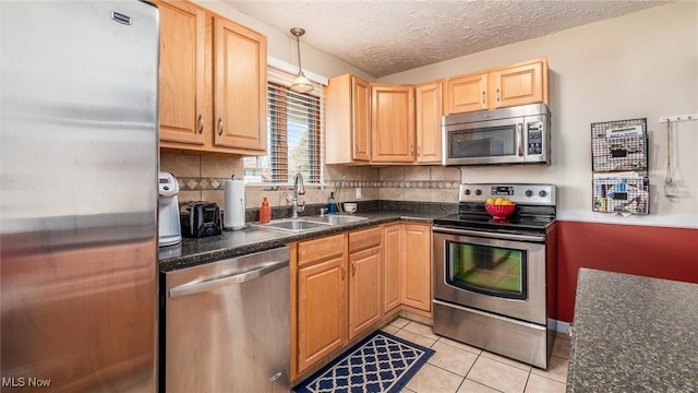 kitchen featuring light tile patterned floors, stainless steel appliances, dark countertops, and a sink