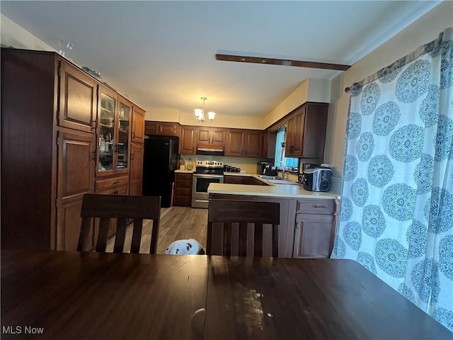 kitchen featuring electric stove, an inviting chandelier, freestanding refrigerator, a sink, and under cabinet range hood