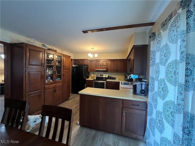 kitchen featuring freestanding refrigerator, light countertops, stainless steel range with electric cooktop, light wood-type flooring, and a notable chandelier