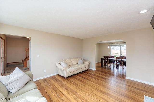 living room with stairs, light wood-type flooring, arched walkways, and baseboards