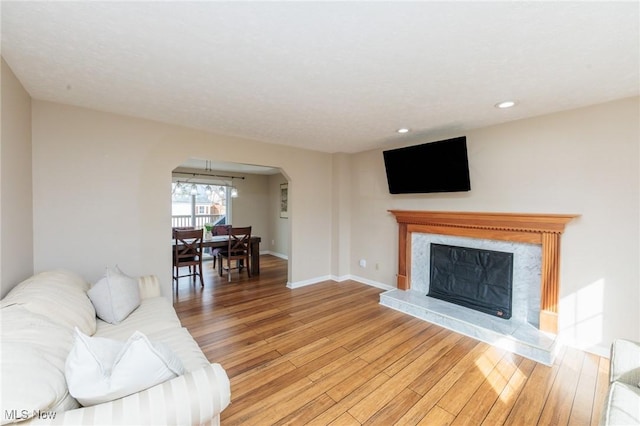 living room with arched walkways, recessed lighting, a premium fireplace, baseboards, and light wood-style floors