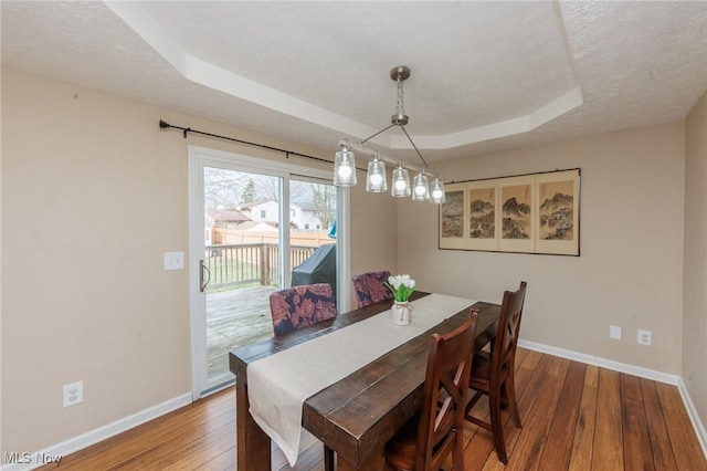 dining space featuring hardwood / wood-style flooring, baseboards, a tray ceiling, and a textured ceiling