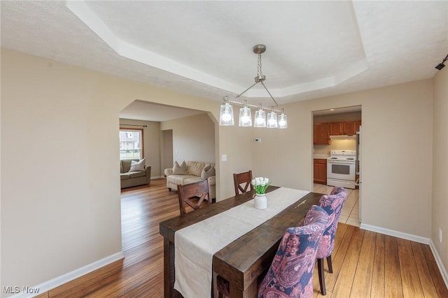 dining space with a tray ceiling, light wood-style floors, and baseboards