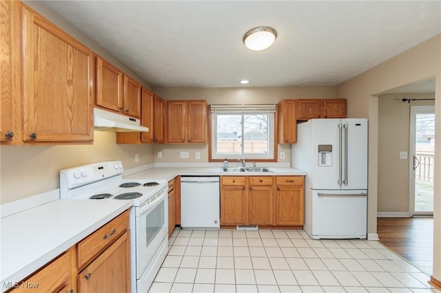 kitchen featuring under cabinet range hood, white appliances, a sink, light countertops, and plenty of natural light