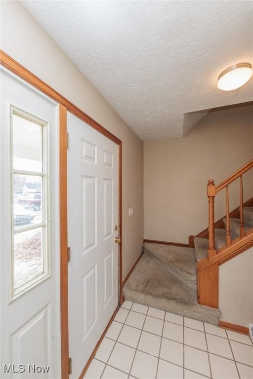 entryway featuring light carpet, baseboards, stairway, and a textured ceiling