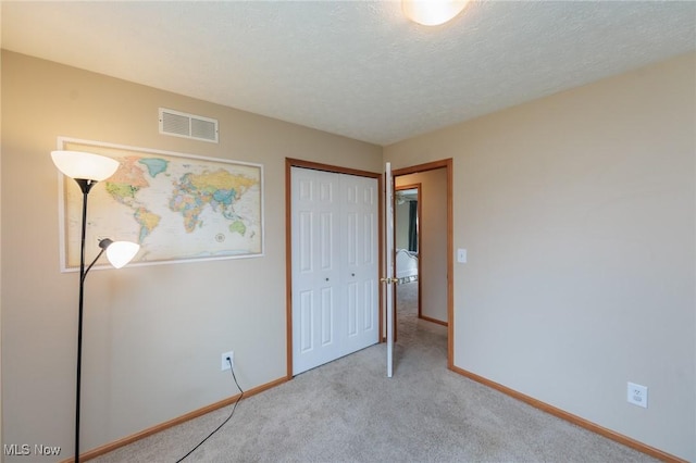 unfurnished bedroom with a textured ceiling, carpet flooring, visible vents, baseboards, and a closet