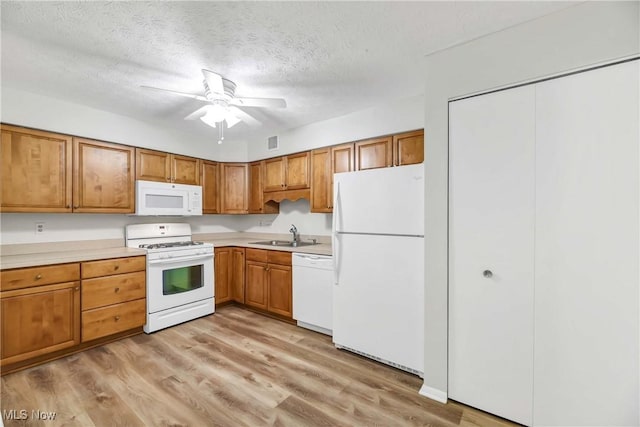 kitchen with brown cabinets, light countertops, light wood-style floors, a textured ceiling, and white appliances