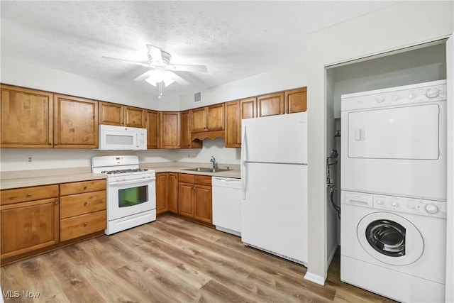 kitchen featuring white appliances, stacked washer and dryer, brown cabinets, light wood-style floors, and a sink