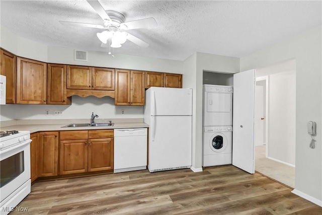 kitchen featuring white appliances, stacked washer and dryer, visible vents, brown cabinetry, and a sink