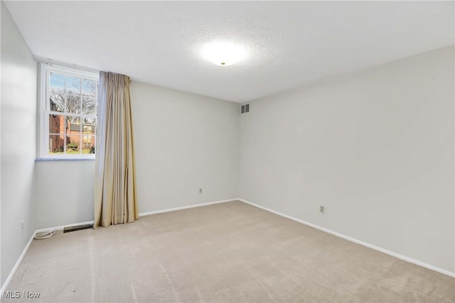 empty room featuring light carpet, a textured ceiling, visible vents, and baseboards