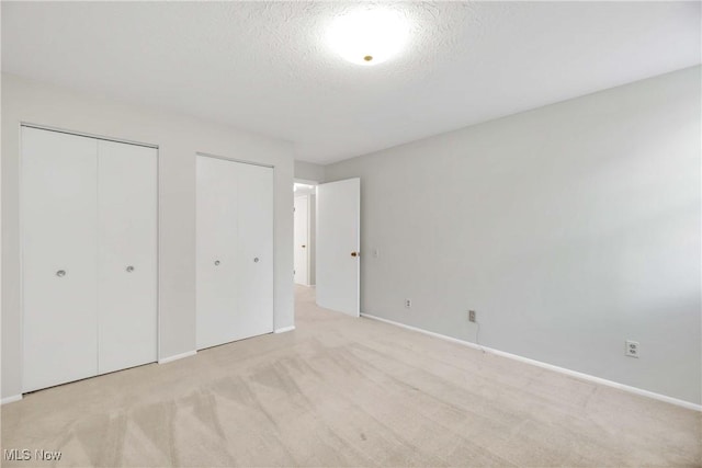 unfurnished bedroom featuring multiple closets, baseboards, a textured ceiling, and light colored carpet