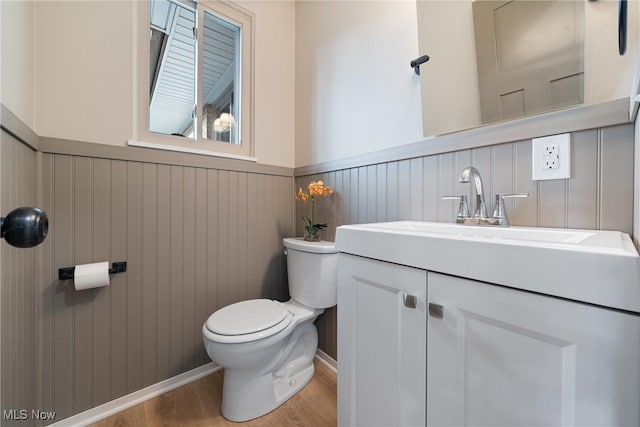 half bathroom featuring toilet, a wainscoted wall, wood finished floors, and vanity