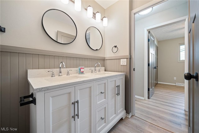 full bathroom with double vanity, visible vents, a sink, and wood finished floors