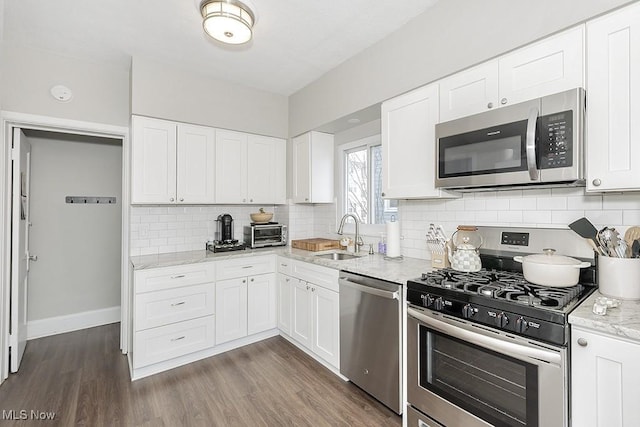 kitchen with decorative backsplash, light stone counters, dark wood-style flooring, stainless steel appliances, and a sink