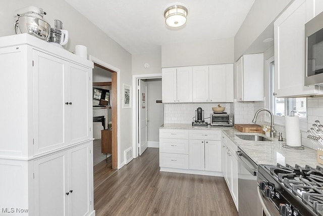 kitchen with stainless steel appliances, visible vents, decorative backsplash, a sink, and wood finished floors