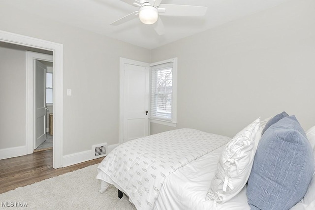 bedroom with a ceiling fan, visible vents, baseboards, and wood finished floors