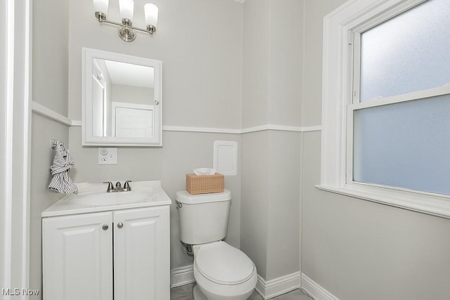 half bathroom with baseboards, vanity, and toilet