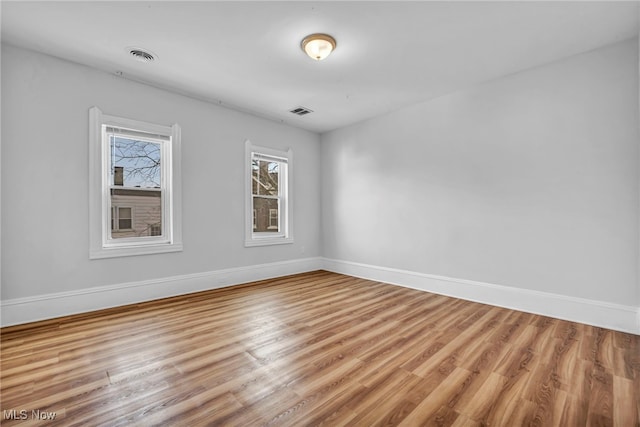 empty room featuring baseboards, visible vents, and wood finished floors