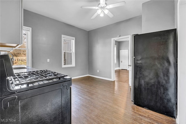 kitchen with wood finished floors, a ceiling fan, baseboards, black range with gas stovetop, and freestanding refrigerator