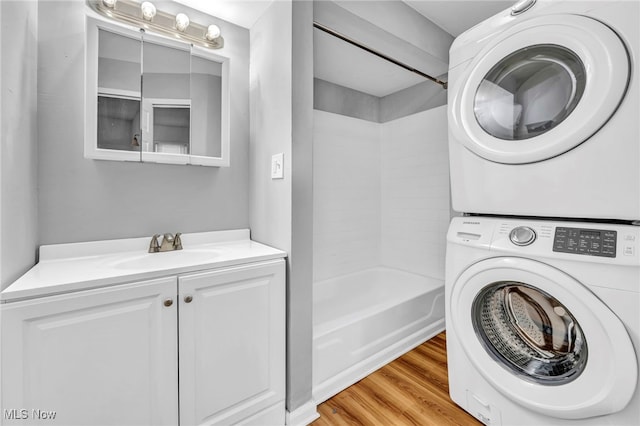 laundry room with laundry area, stacked washer and dryer, a sink, and light wood-style flooring