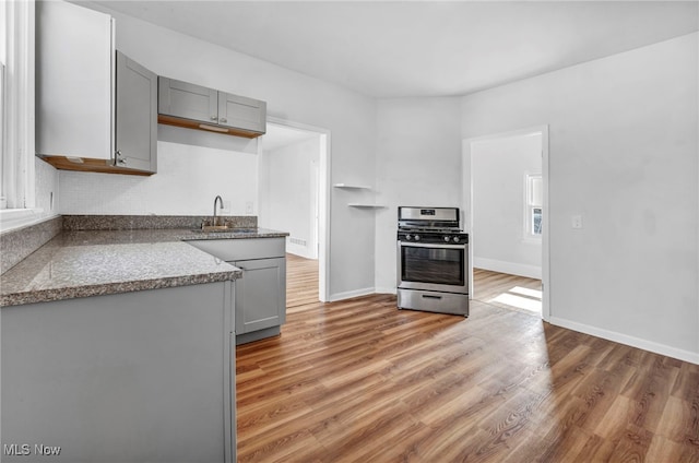 kitchen featuring stainless steel gas range, baseboards, light wood finished floors, and gray cabinetry