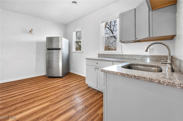 kitchen featuring a sink, light wood-type flooring, freestanding refrigerator, light stone countertops, and tasteful backsplash