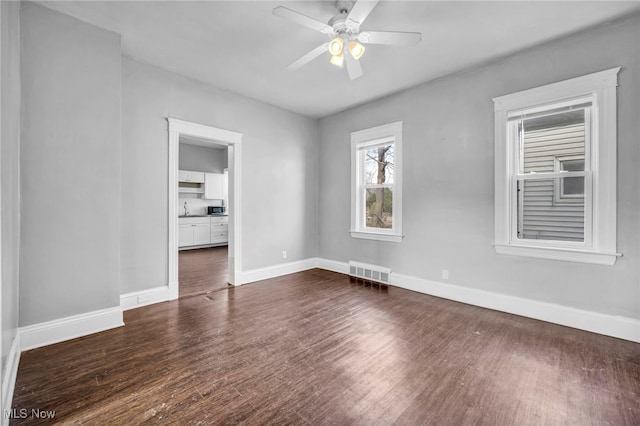 unfurnished room featuring a ceiling fan, visible vents, dark wood finished floors, and baseboards