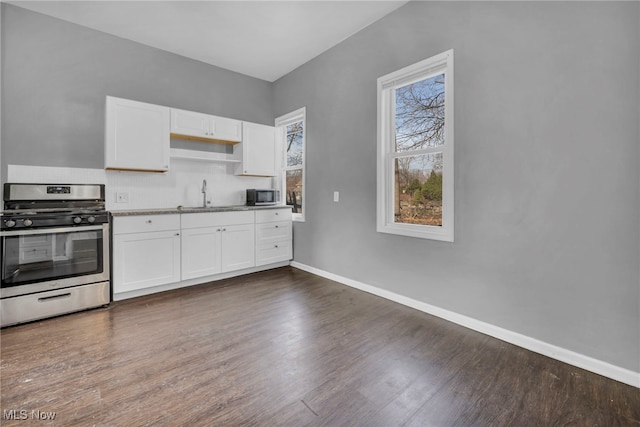 kitchen featuring stainless steel appliances, dark wood-type flooring, white cabinets, a sink, and baseboards