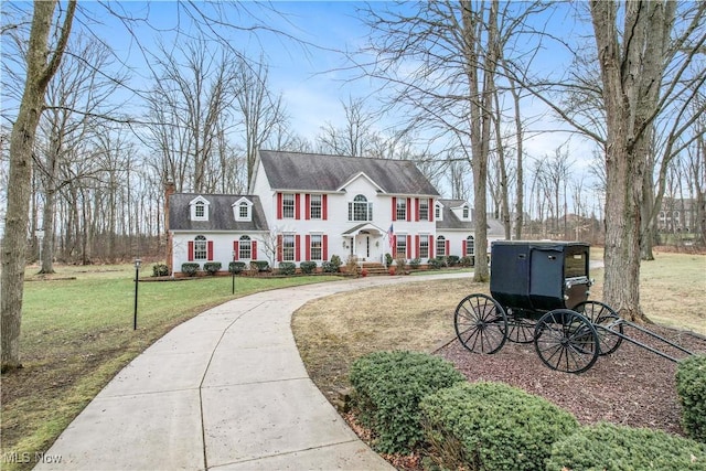 view of front facade featuring a front yard, concrete driveway, and a chimney