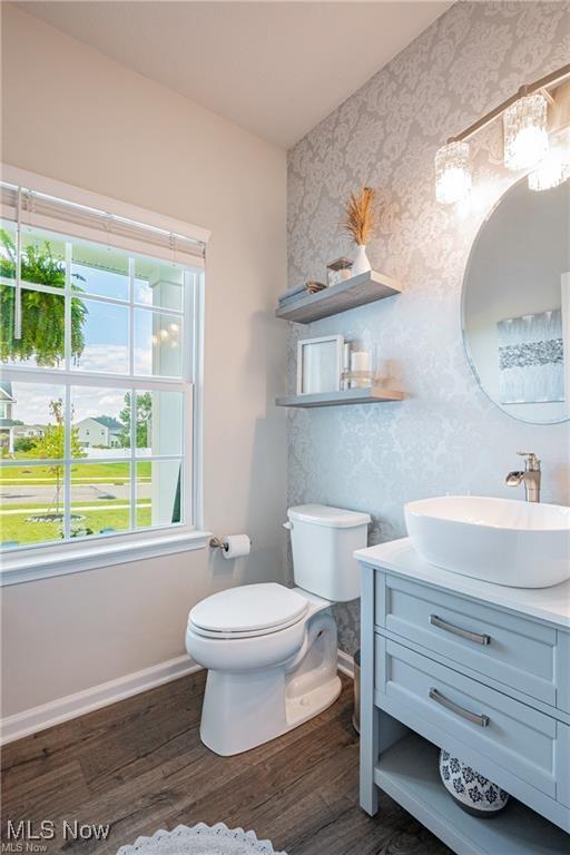 bathroom with toilet, vanity, wood finished floors, baseboards, and wallpapered walls