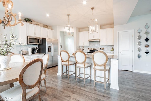 kitchen featuring stainless steel appliances, a breakfast bar area, under cabinet range hood, and light wood finished floors